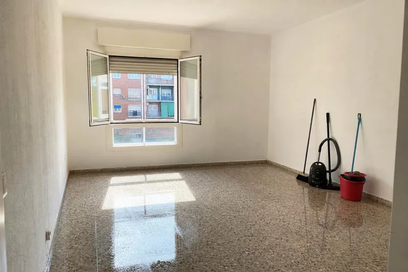 Dormitorio vacío recién fregado, con la fregona, la escoba y el aspirador junto a la pared